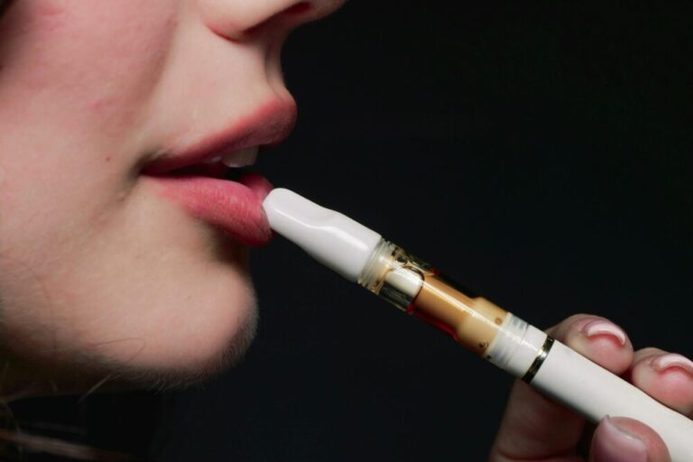 Close-up image of a woman vaping with an e-cigarette on a dark background.