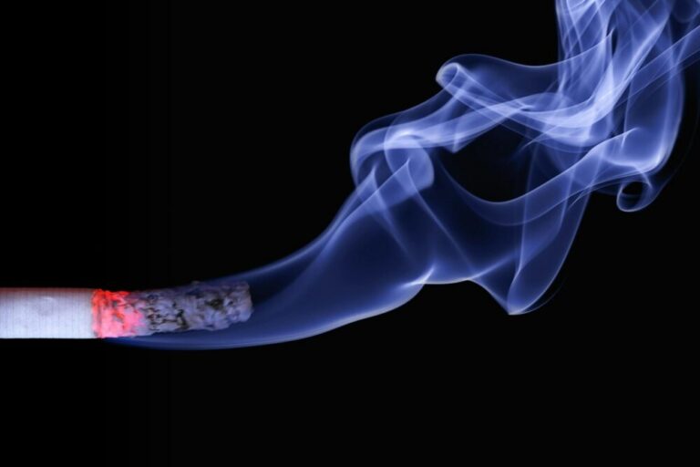 Detailed close-up of a cigarette with glowing ember and swirling smoke on a black background.